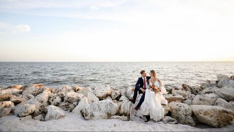 Newly Weds Glaring in each others eyes while sitting on rocks in front of beautiful open water and clear sky